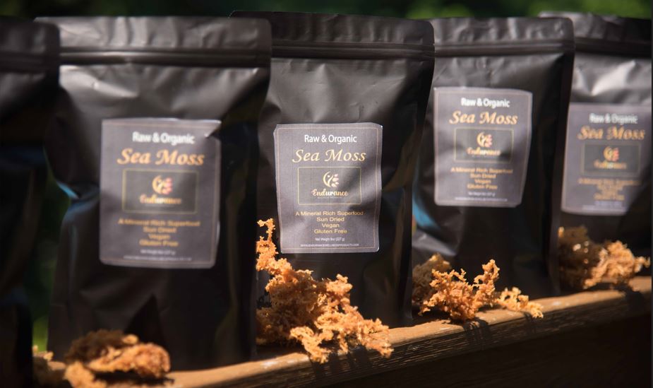 Four front-facing Premium Organic Dried Sea Moss packages displayed side by side with sea moss arranged along the bottom of each package
